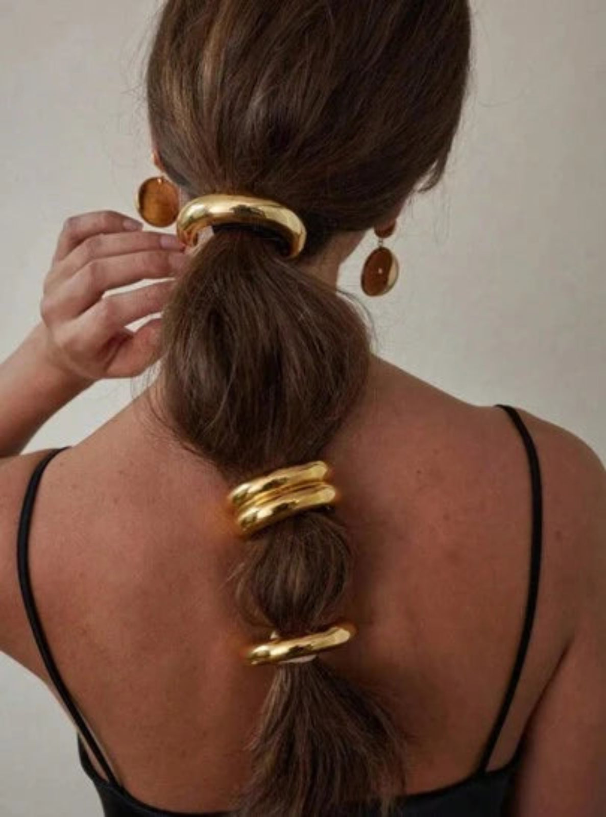Person with a high ponytail wearing gold hair accessories against a neutral background