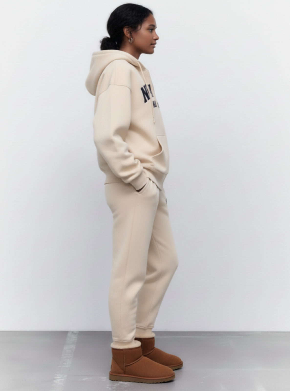 Person wearing a beige hoodie and pants with brown boots on a white background