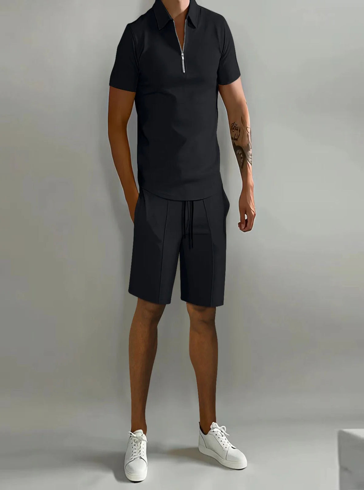 Person wearing a black polo shirt and shorts with white sneakers on a gray background
