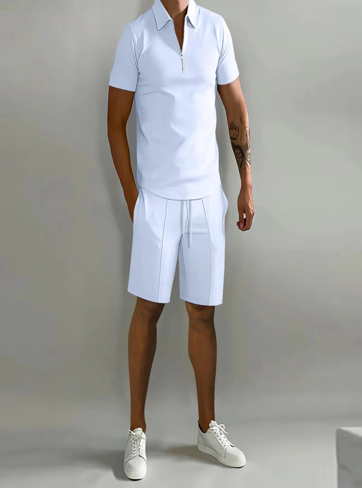 Person wearing a white polo shirt and shorts set with white sneakers on a plain background