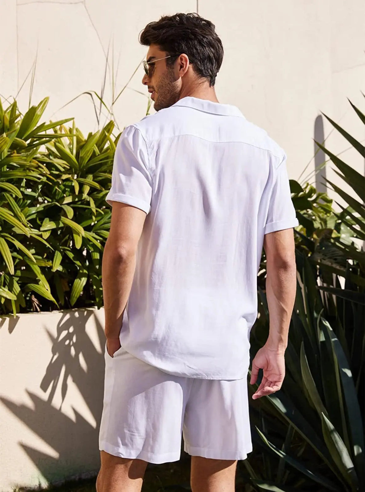 Man wearing a white t-shirt and shorts standing outdoors with plants in the background