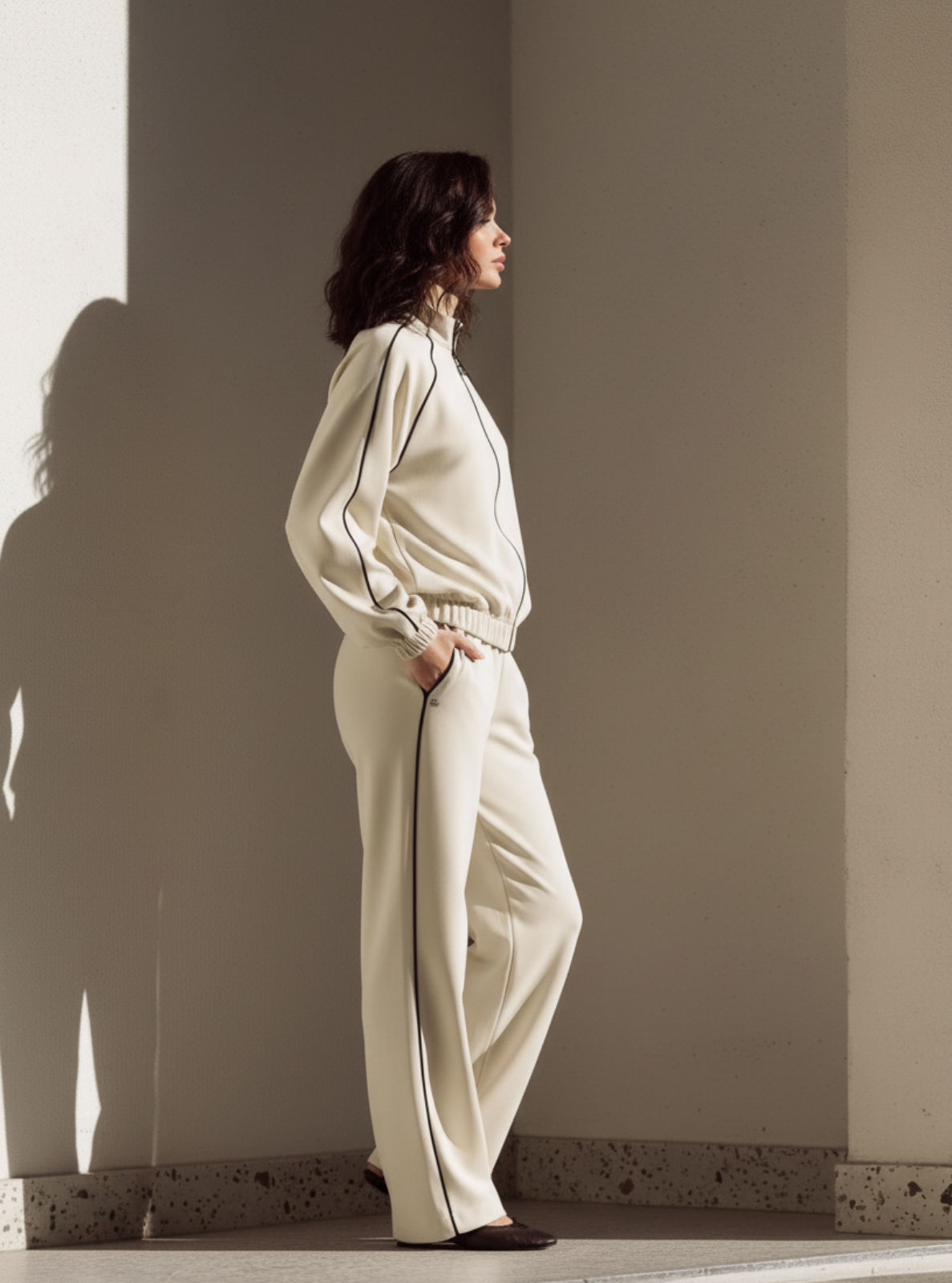 Woman in a white outfit standing against a plain wall.