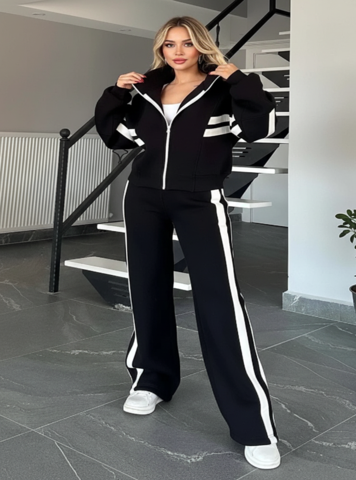 Woman wearing a black tracksuit with white stripes in an indoor setting.
