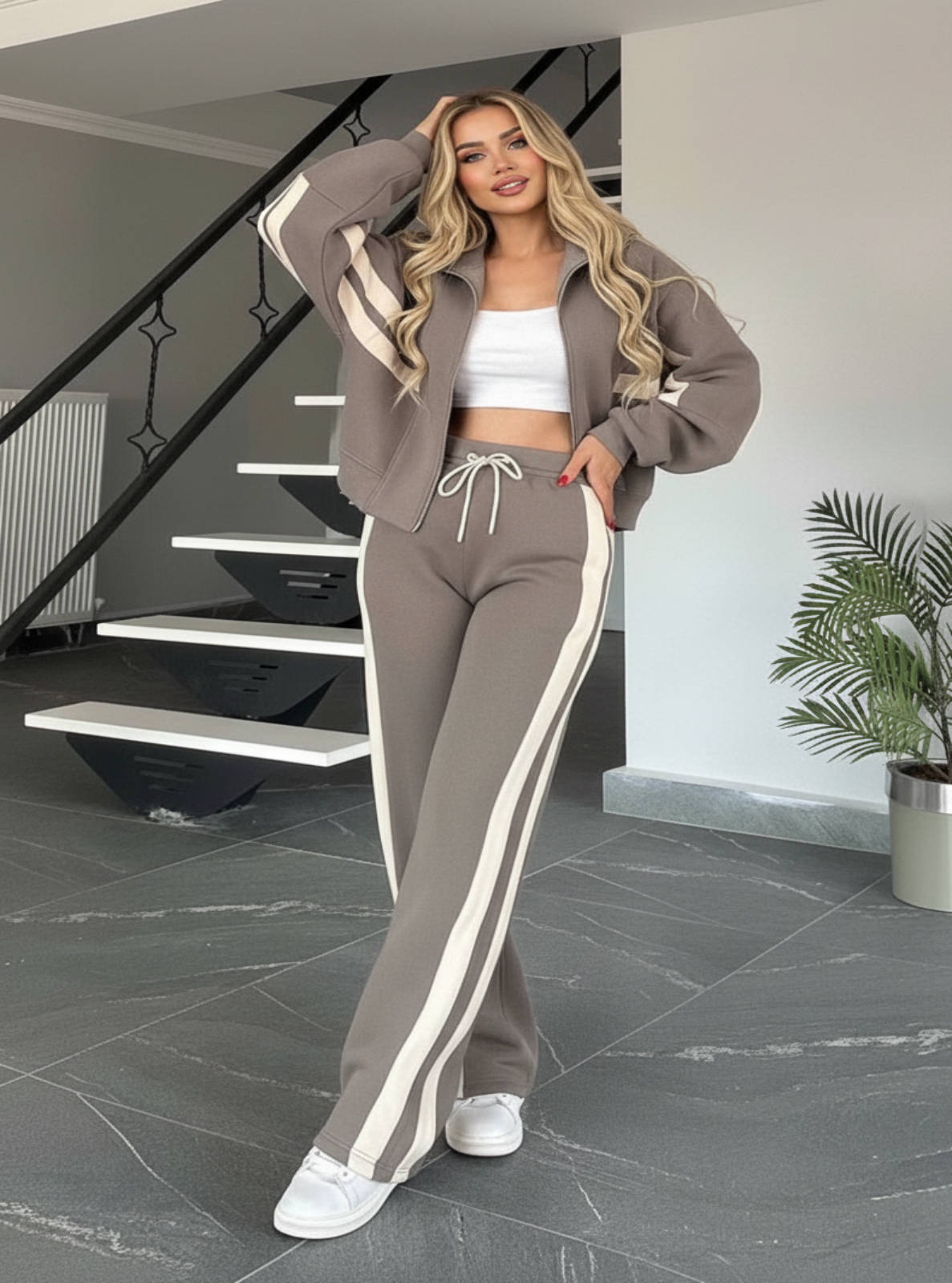 Woman in a gray tracksuit with white stripes standing in a modern interior setting.