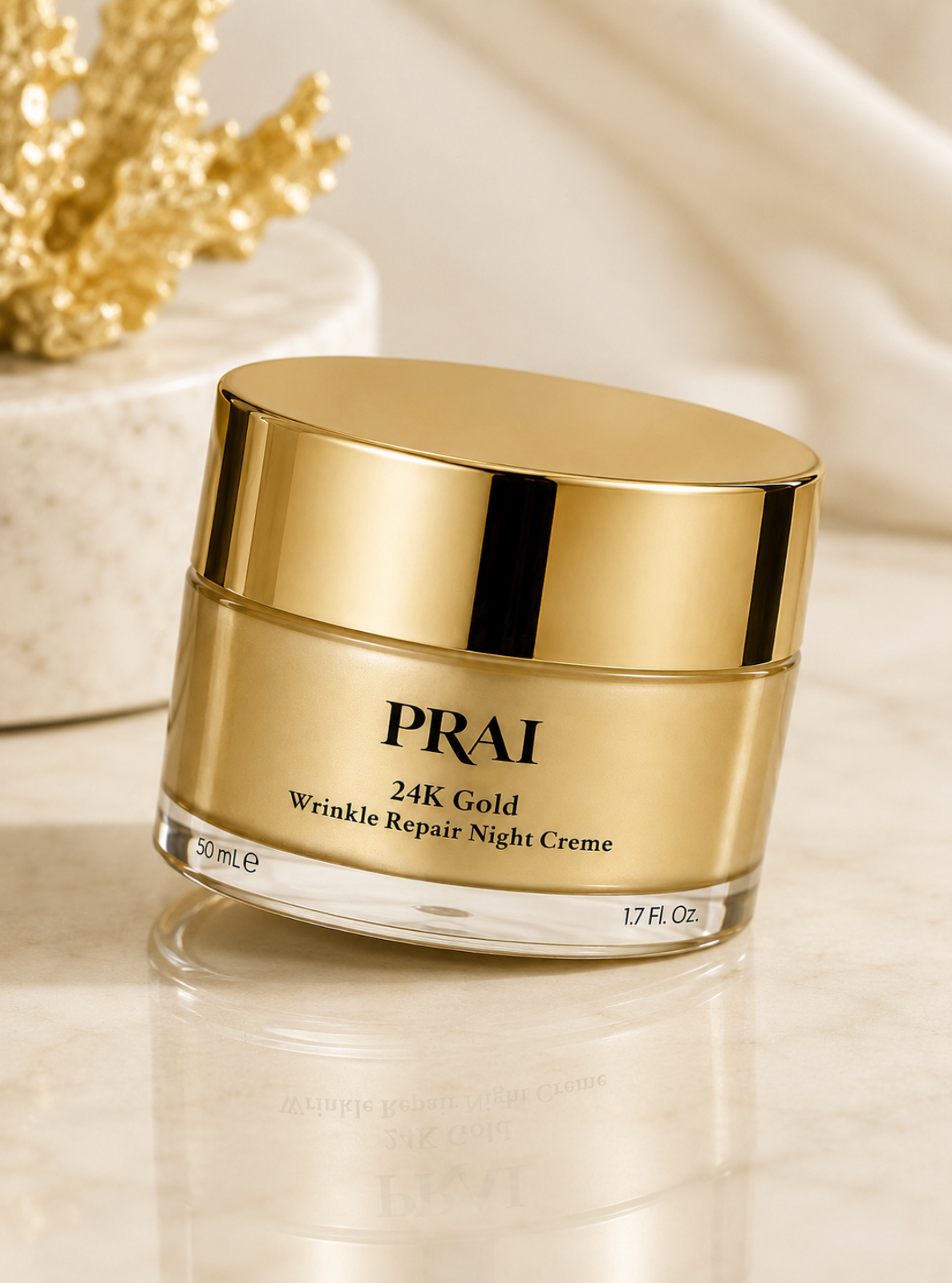 PRAI 24K Gold Wrinkle Repair Night Creme in a gold jar with a reflective lid, set on a marble surface with a gold decorative branch in the background.