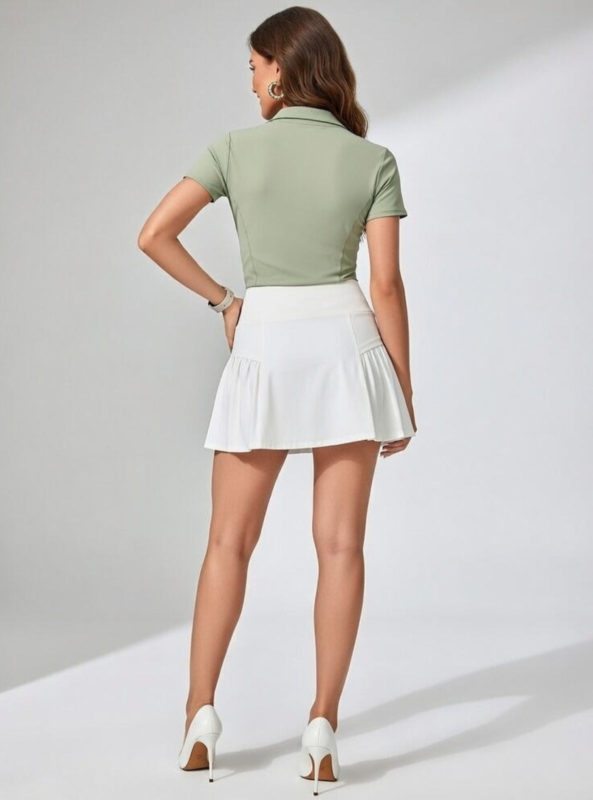 Woman wearing a green polo shirt and white skirt on a plain background