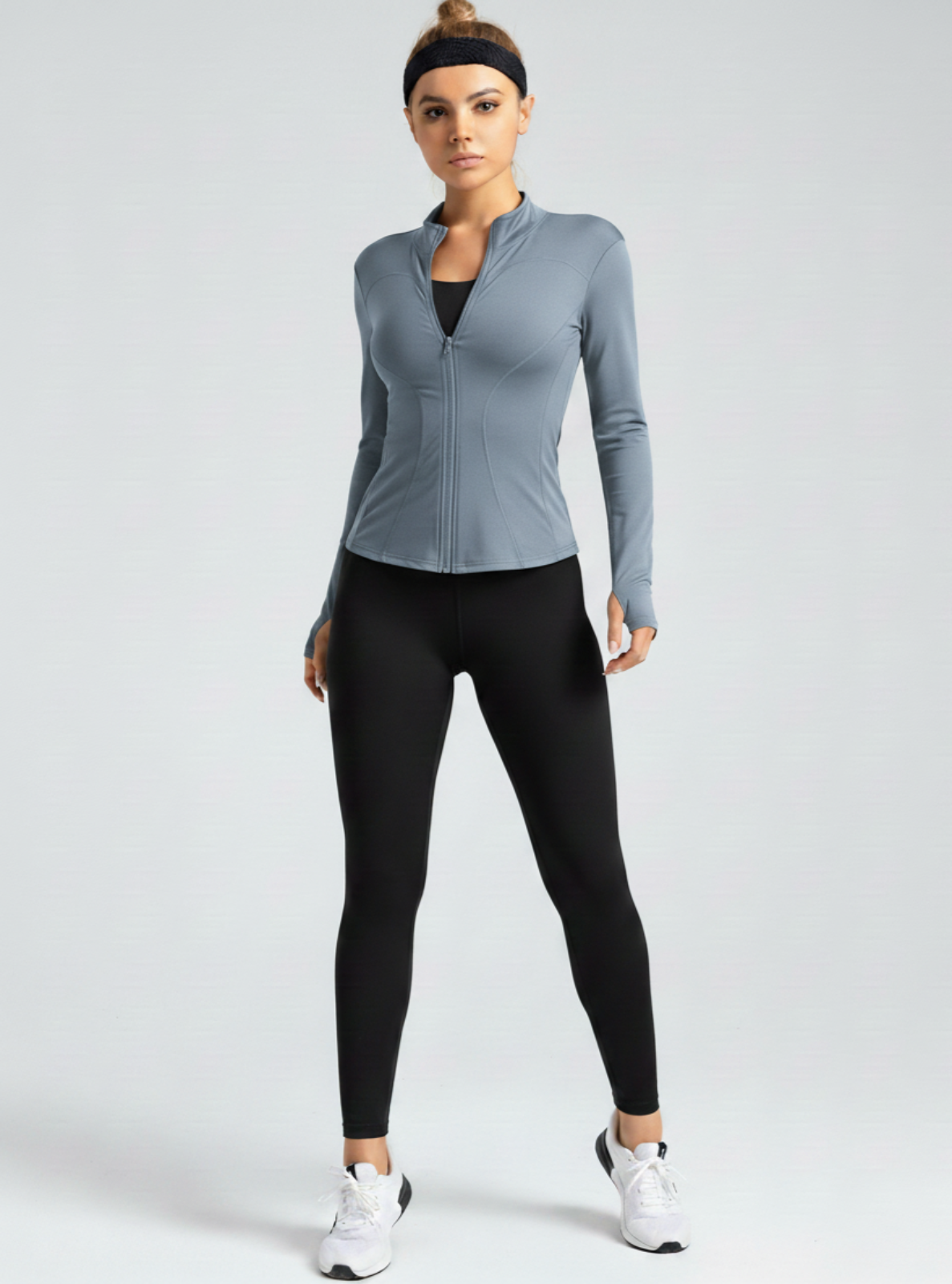 Woman wearing a gray long-sleeve athletic jacket and black leggings on a white background