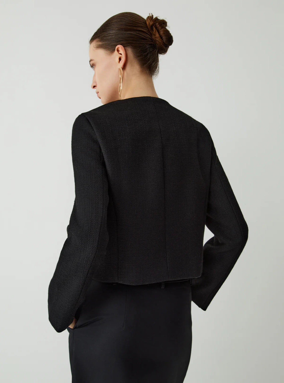 Backside of black textured Jacket on a model facing a white background