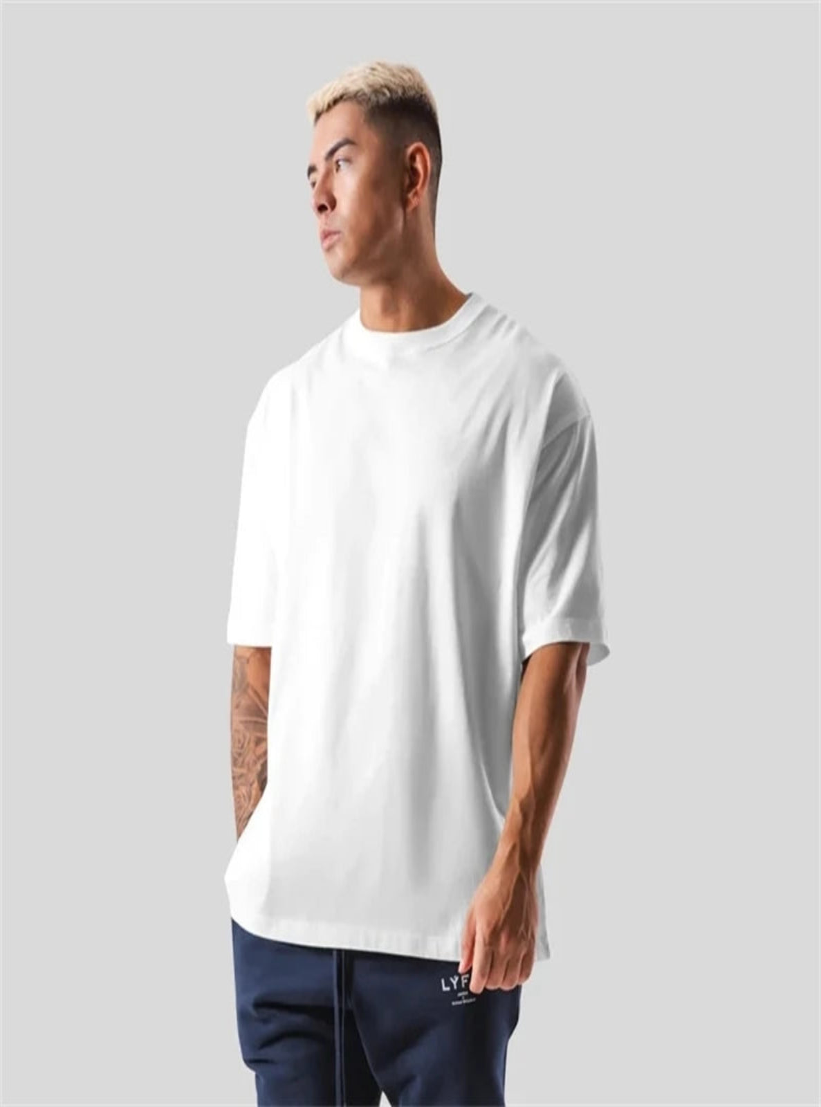 Man wearing a plain white t-shirt and dark pants on a light gray background