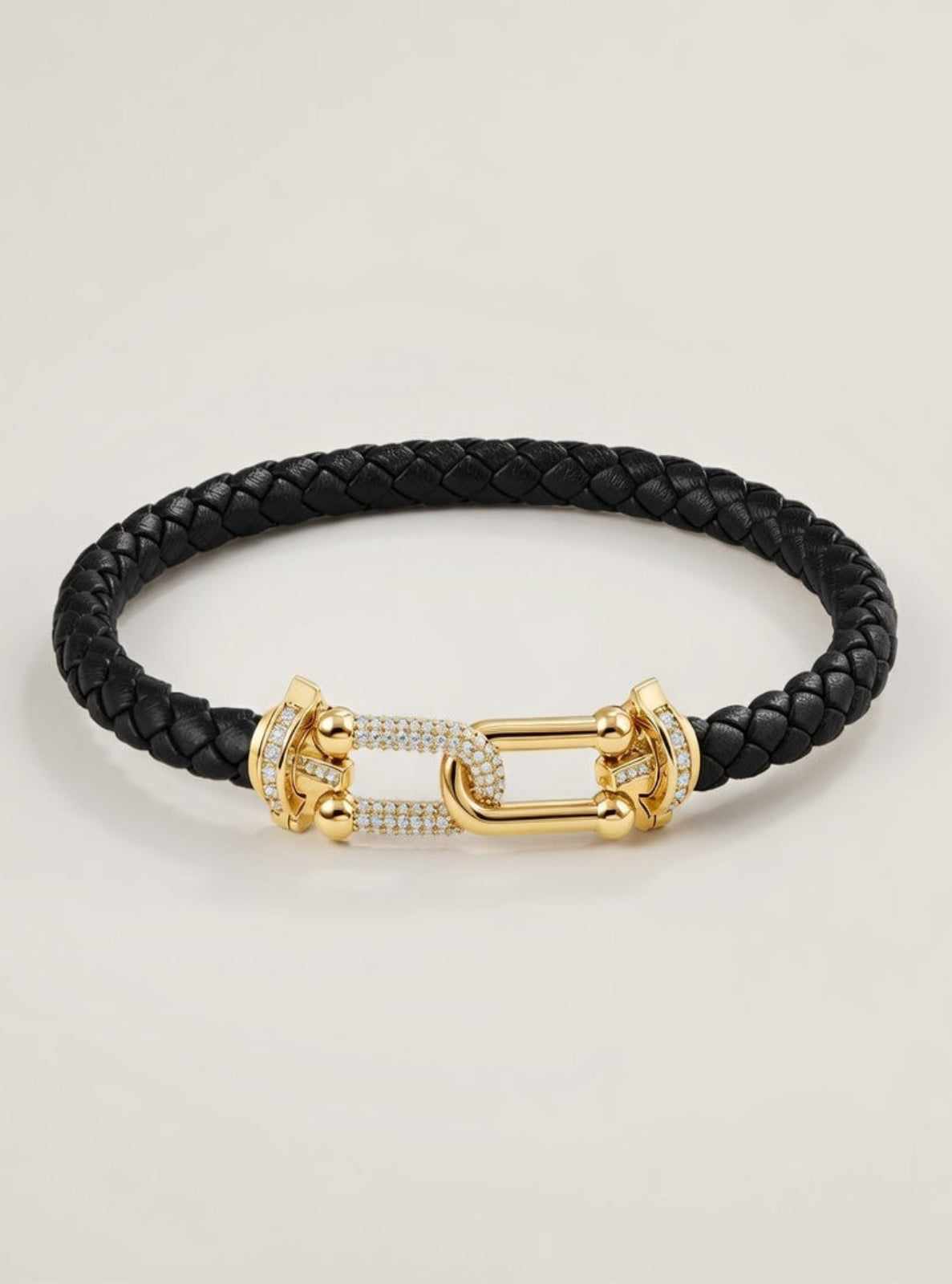 Black braided leather bracelet with gold clasp on a light beige background