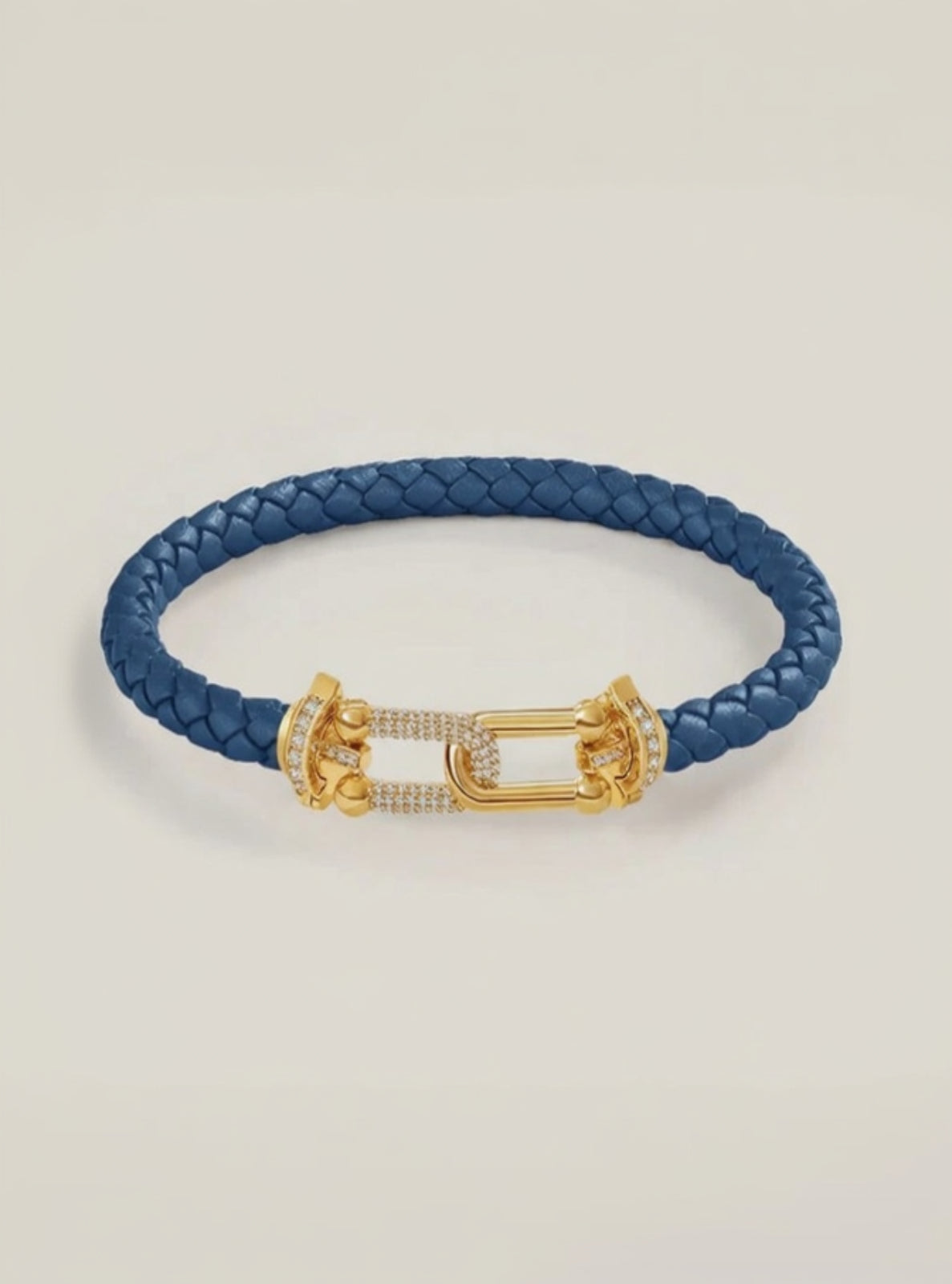 Blue braided leather bracelet with a gold clasp on a light beige background