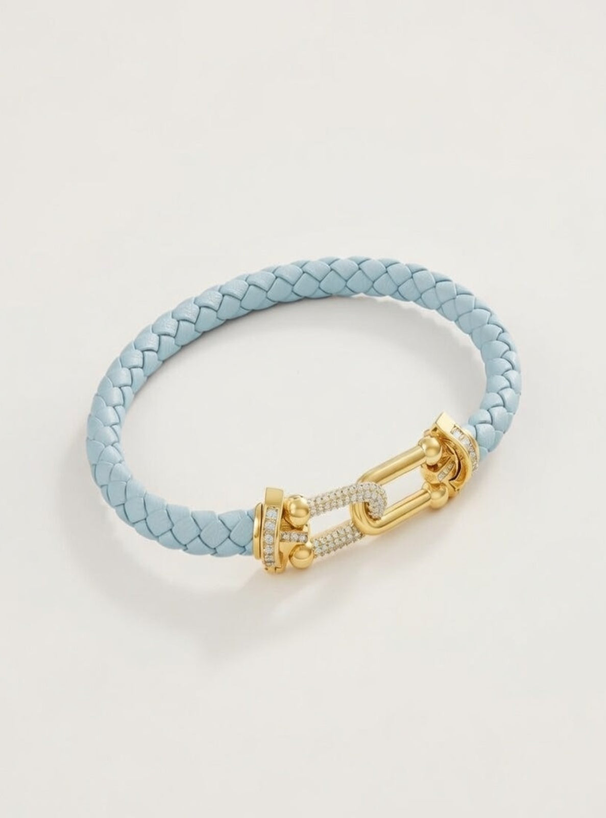 Light blue braided leather bracelet with a gold clasp on a light gray background