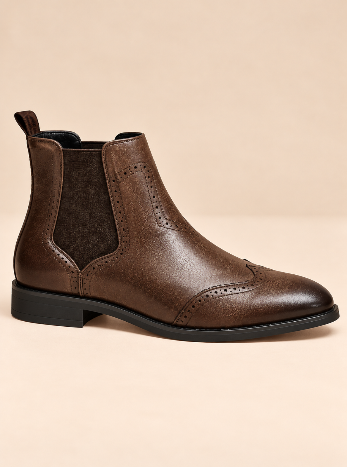 A dark brown leather Chelsea boot with a pull tab, brogue detailing, and a black elastic side panel, shown against a solid beige background.
