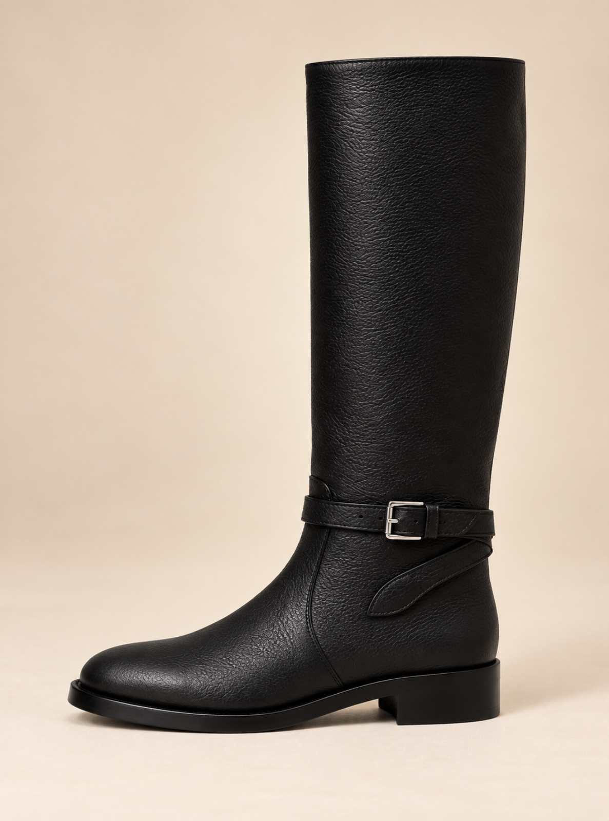 A single black leather knee-high boot with a side buckle strap, shown in profile against a solid beige background.