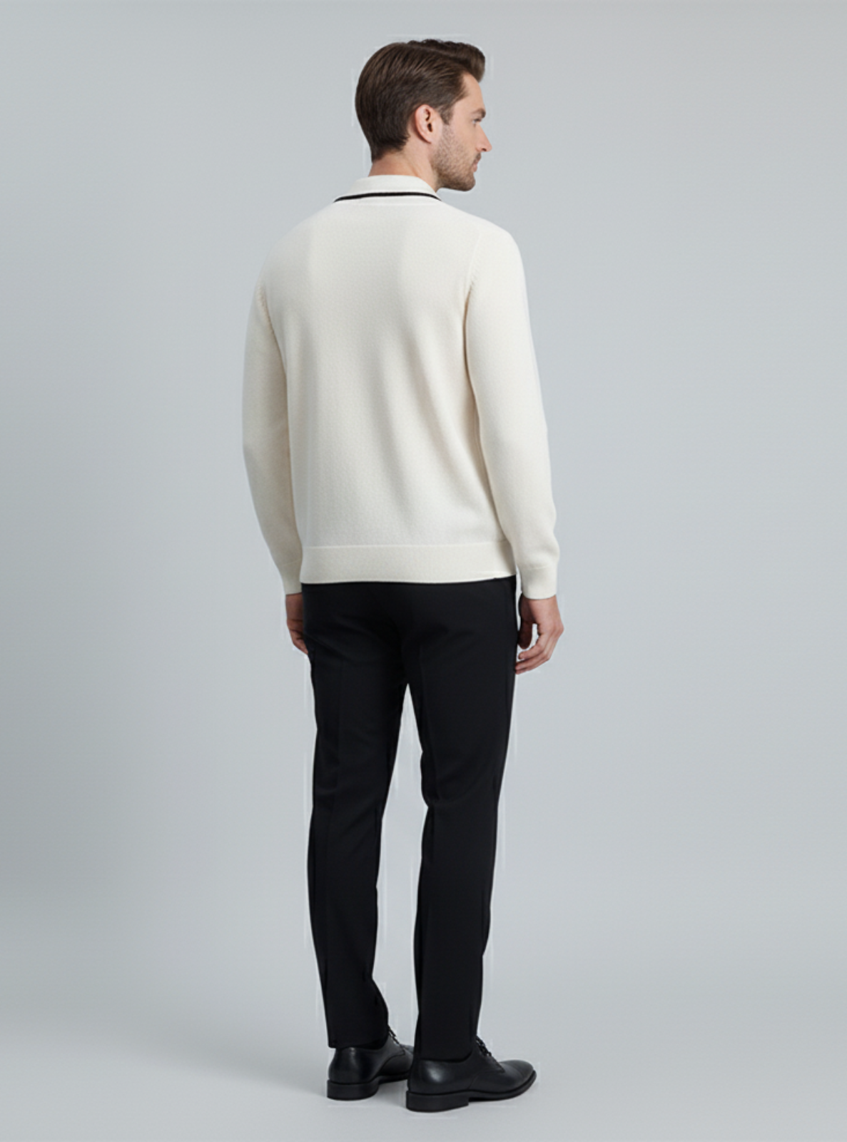 Man wearing a cream sweater and black pants on a gray background