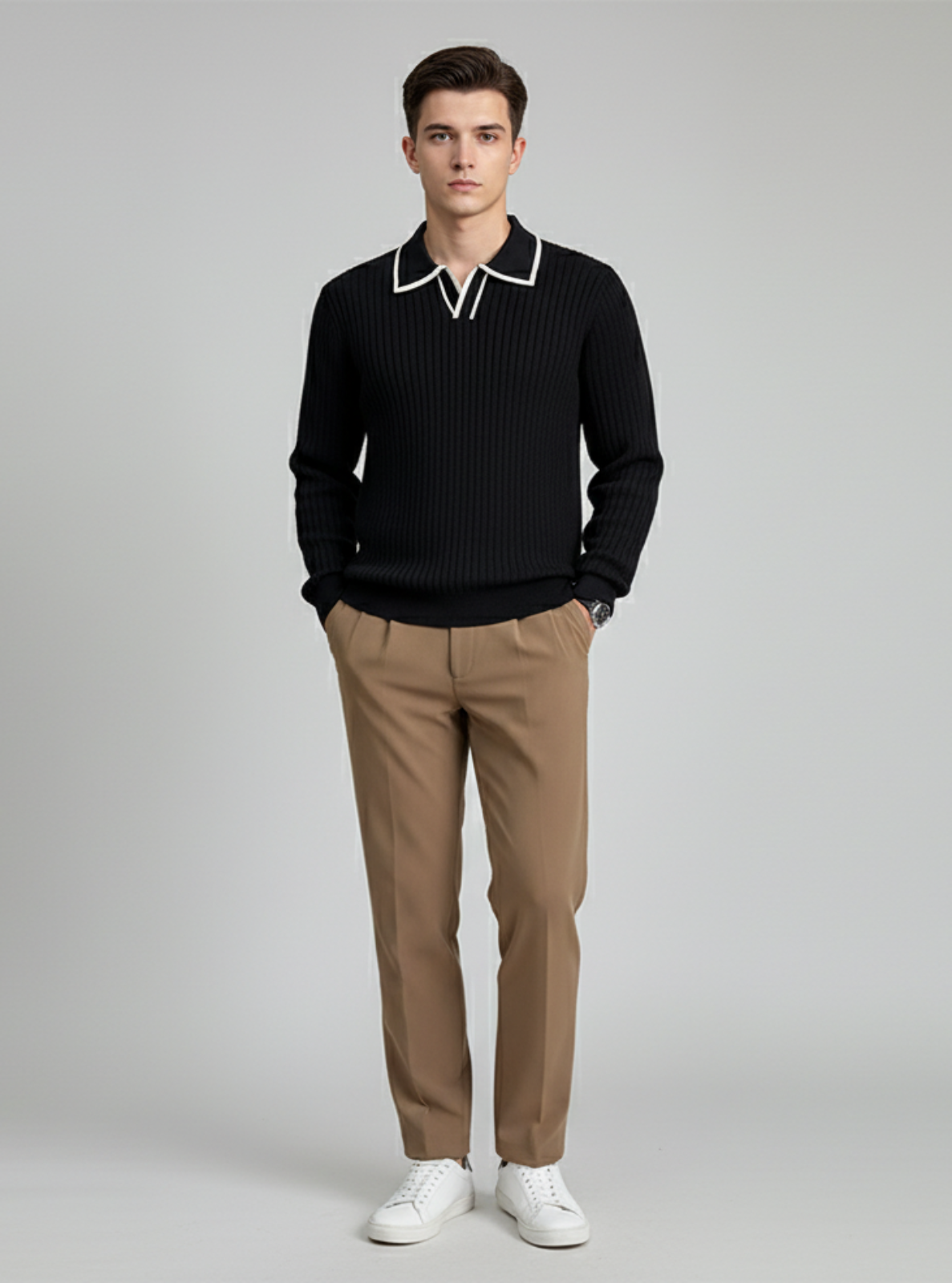 Man wearing a black sweater with white trim, beige pants, and white shoes on a gray background