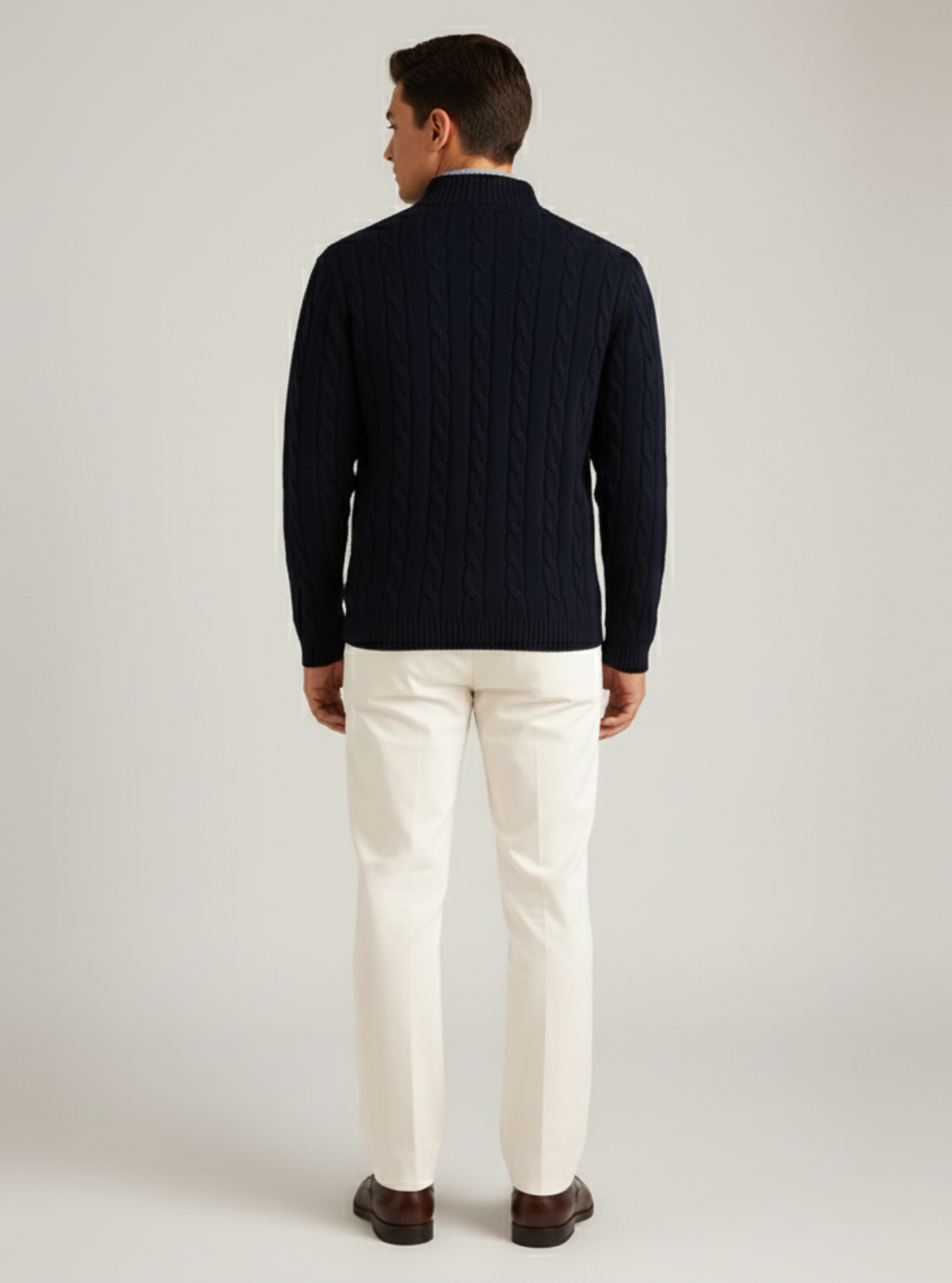 Man wearing a navy sweater and white pants on a light gray background