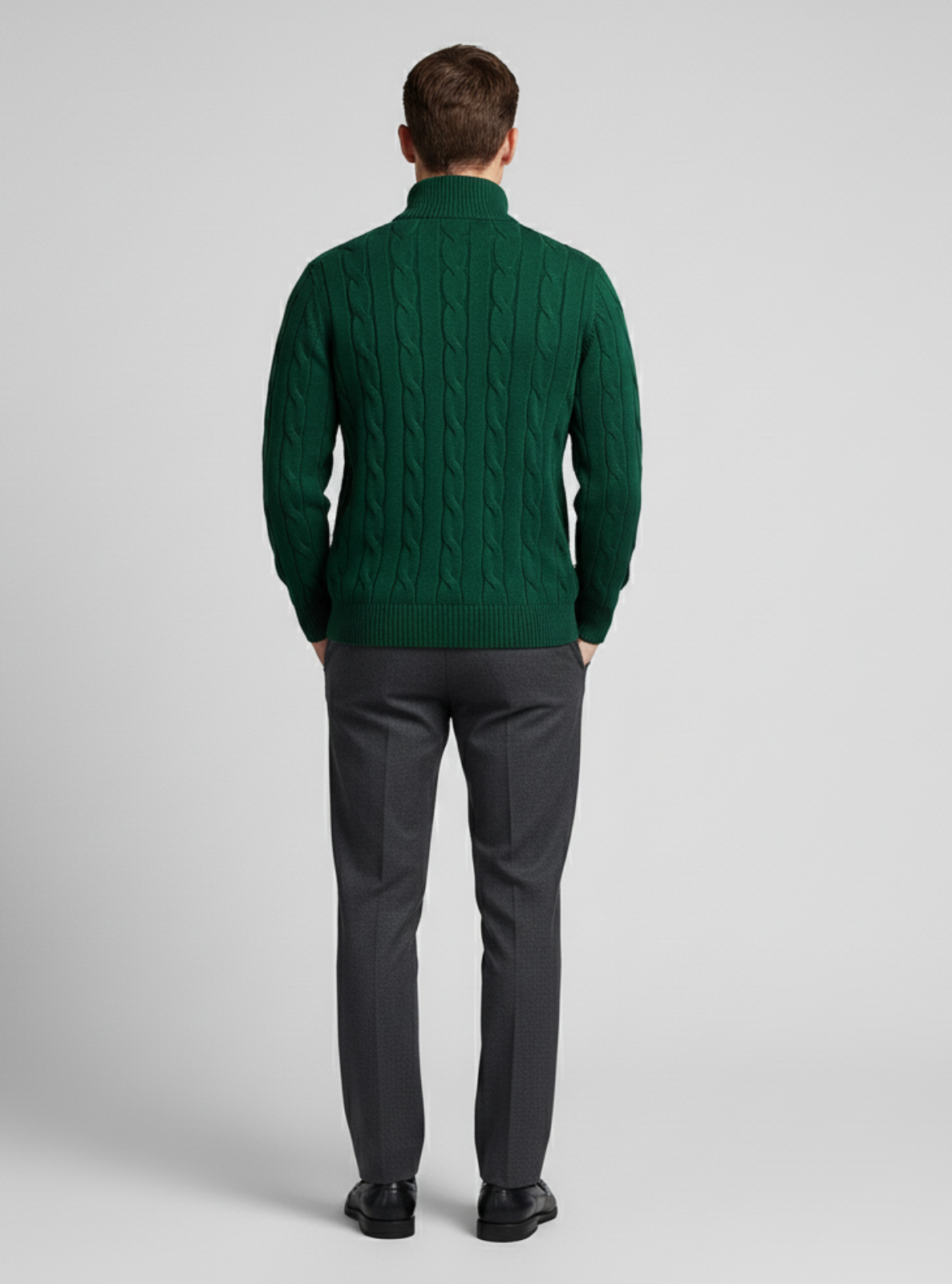 Man wearing a green cable knit sweater and dark gray pants on a light gray background