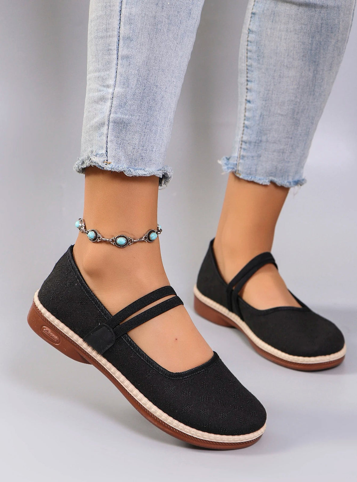 Black flat shoes worn with light blue jeans on a gray background