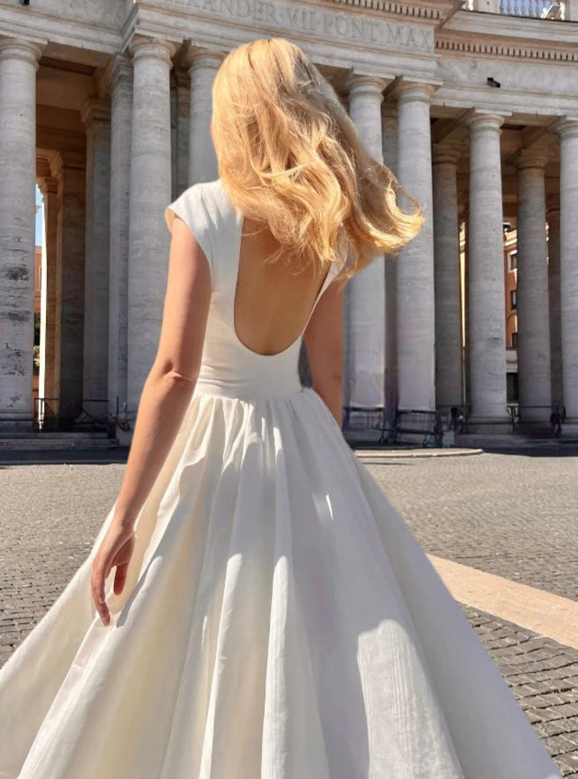 Woman in a white dress standing in front of a classical building with columns.