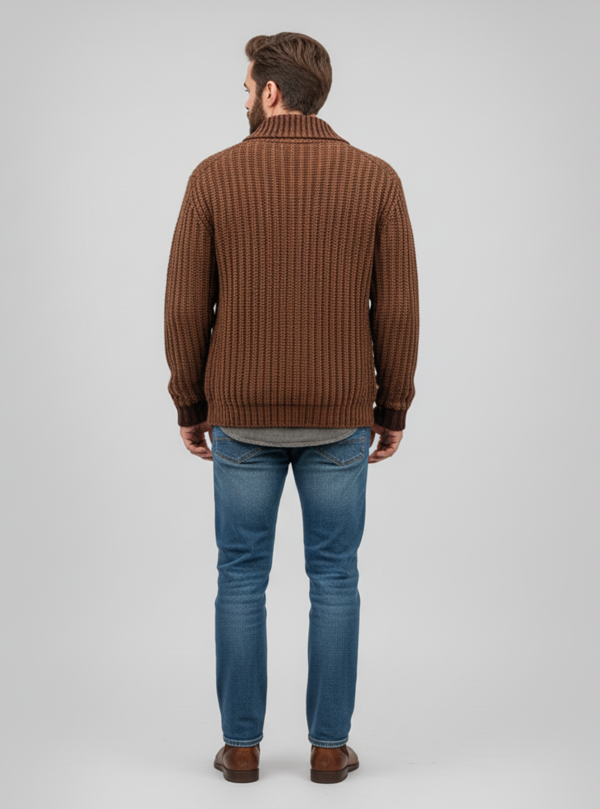 Man wearing a brown textured sweater and blue jeans on a gray background