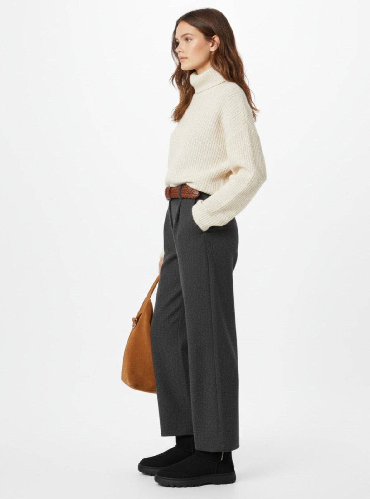 Woman wearing a white turtleneck sweater and dark pants with a brown bag on a white background