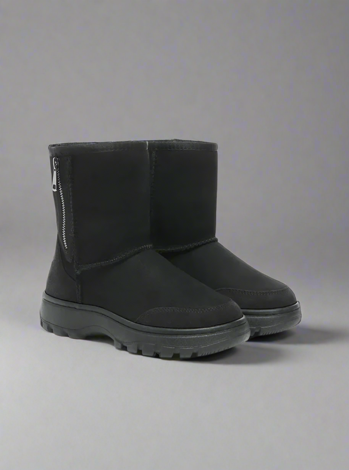 Black winter boots with zippers on a gray background