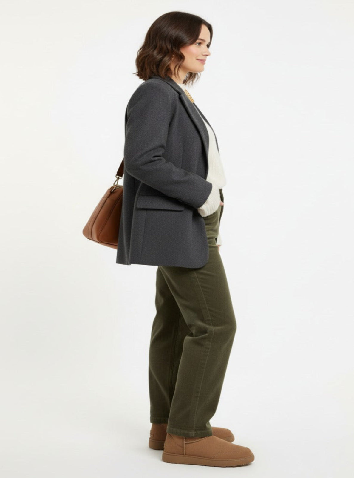 Woman wearing a gray blazer, white shirt, green pants, and brown boots on a white background