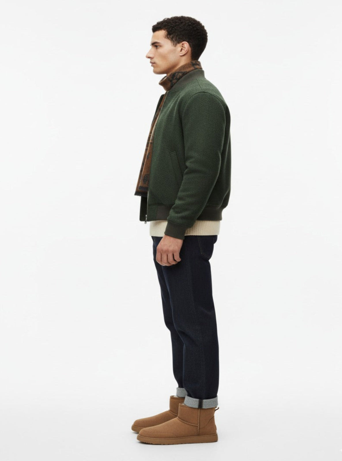 Man wearing a green jacket, beige shirt, black pants, and brown boots on a white background