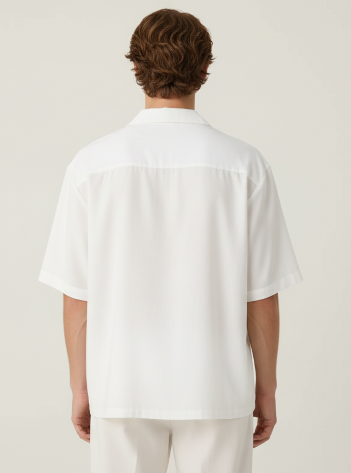 Man wearing a white shirt and pants against a plain background