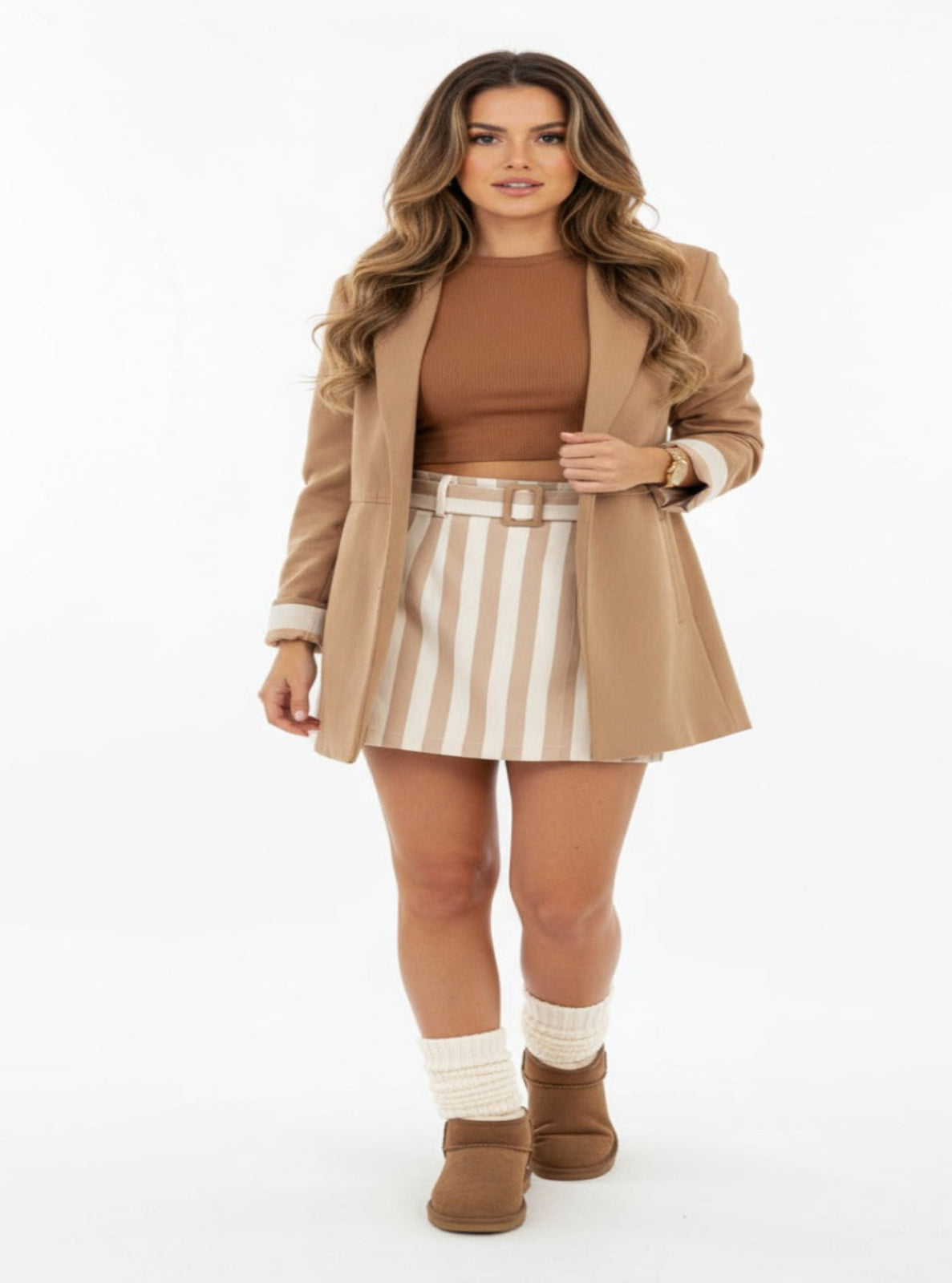 Woman wearing a brown coat, brown top, striped skirt, and brown boots on a white background