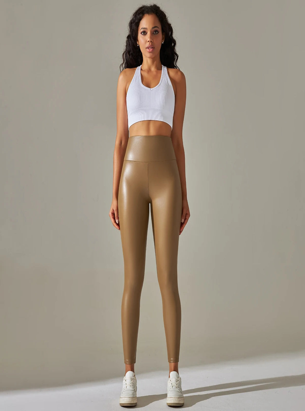 Woman wearing a white sports bra and brown leggings against a beige background