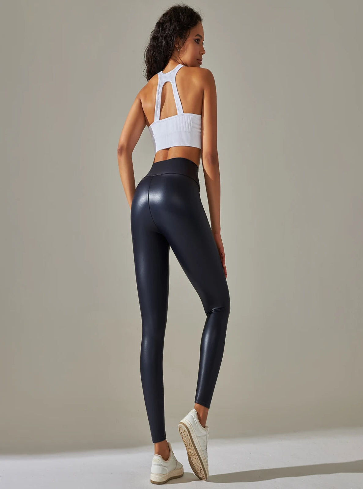 Woman wearing black leggings and a white sports bra against a neutral background