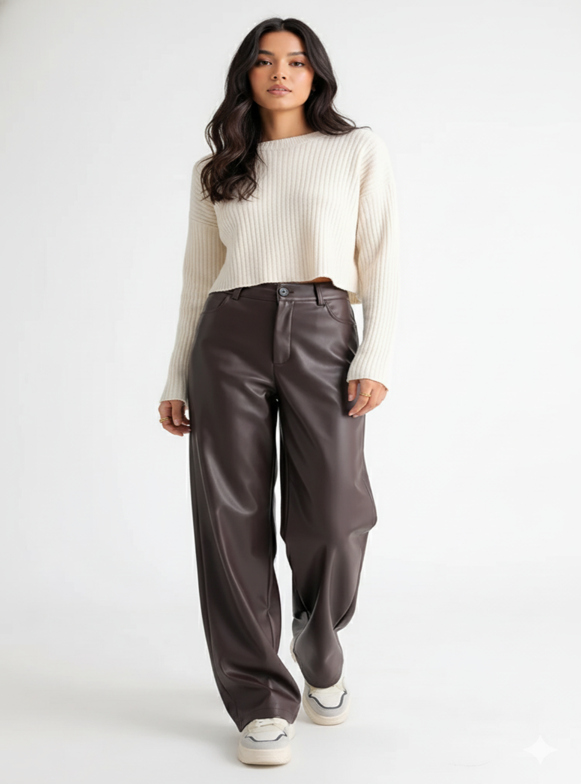 Woman wearing a cream sweater and brown leather pants on a white background