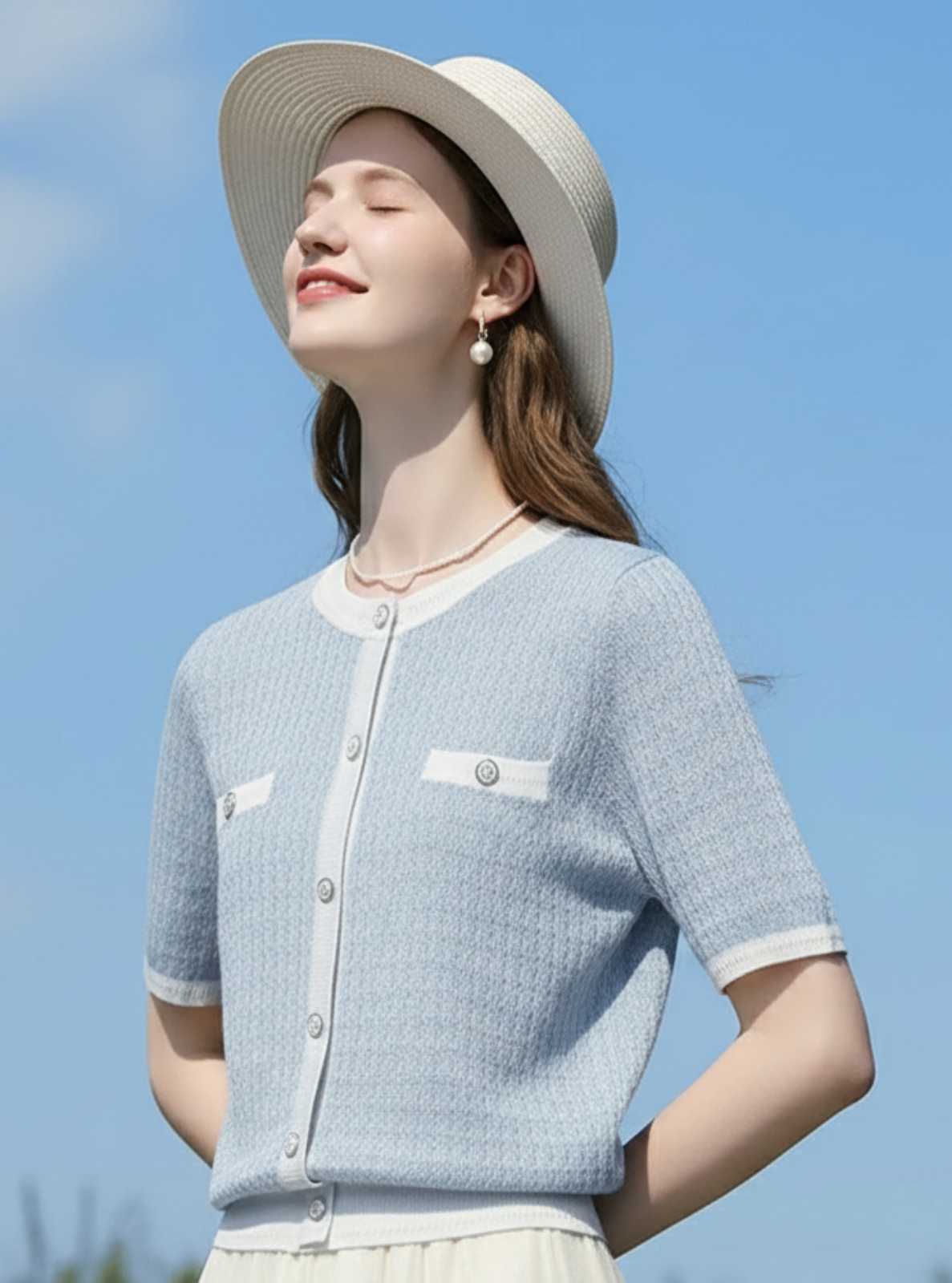 Woman wearing a light blue cardigan and white hat against a clear blue sky.