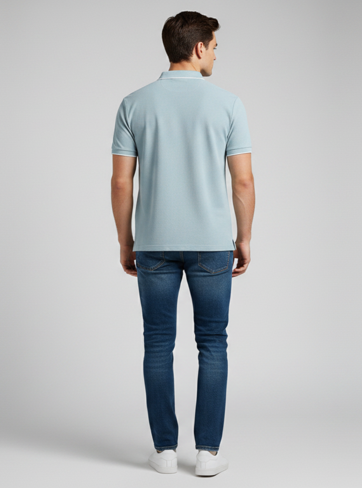 Man wearing a light blue polo shirt and dark blue jeans on a gray background
