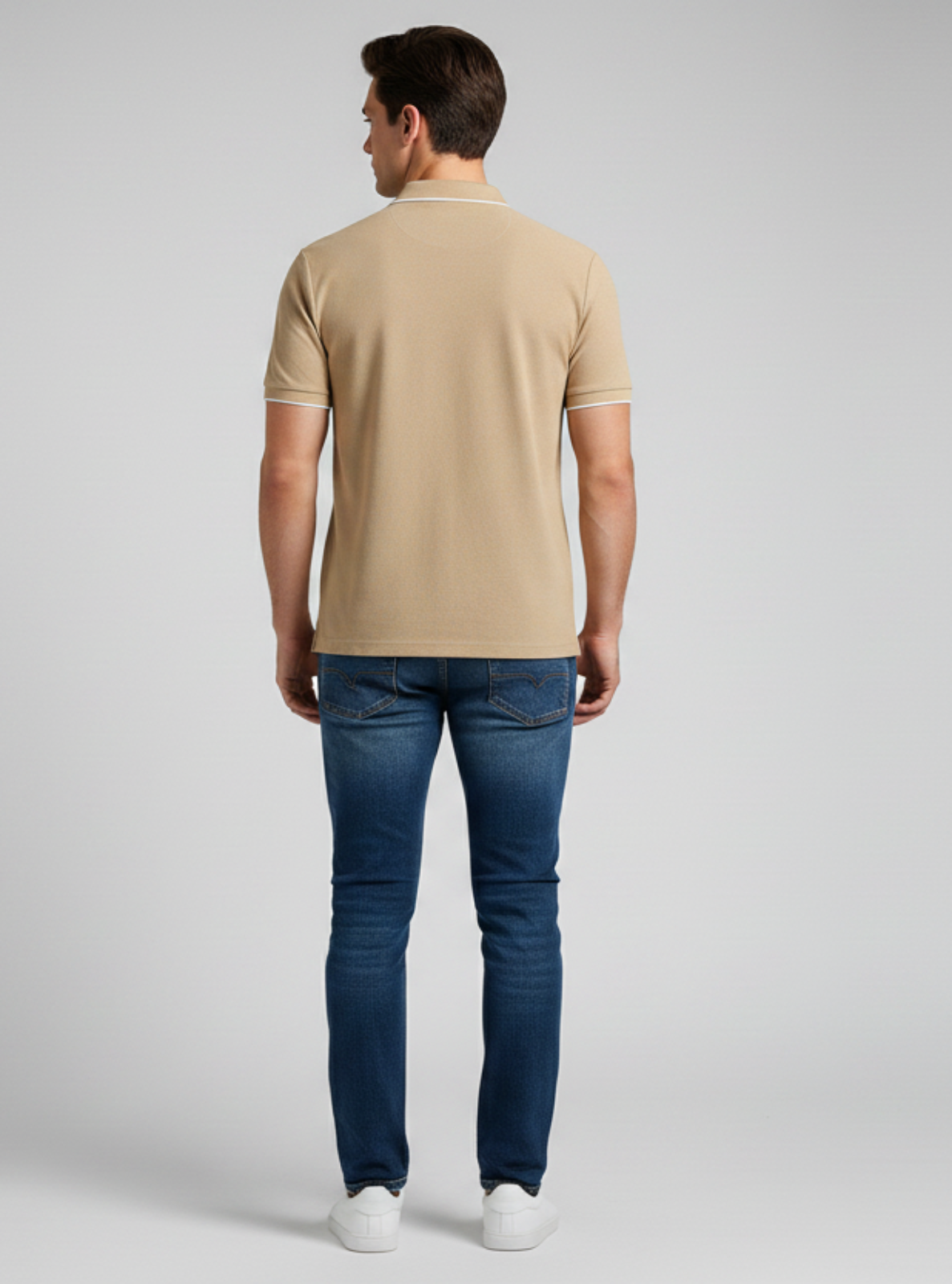Man wearing a beige polo shirt and blue jeans on a gray background
