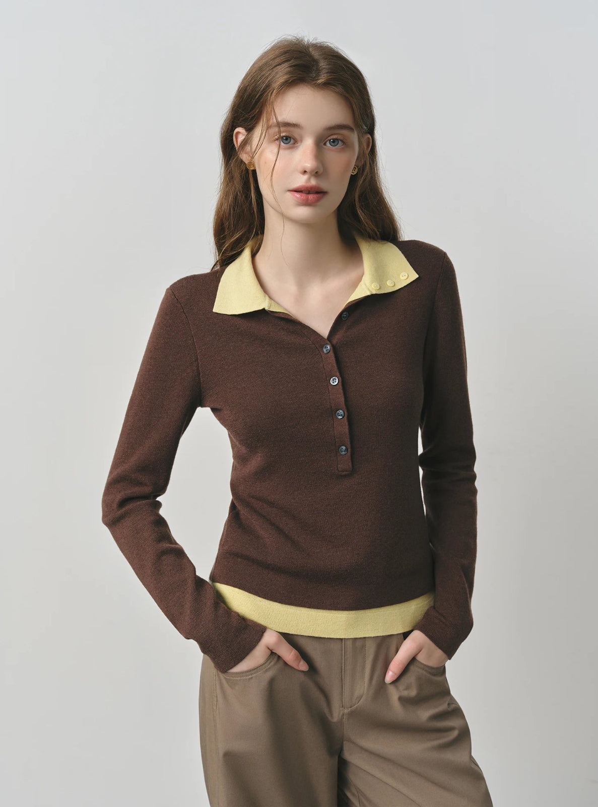 Woman wearing a brown sweater with a yellow collar against a plain background