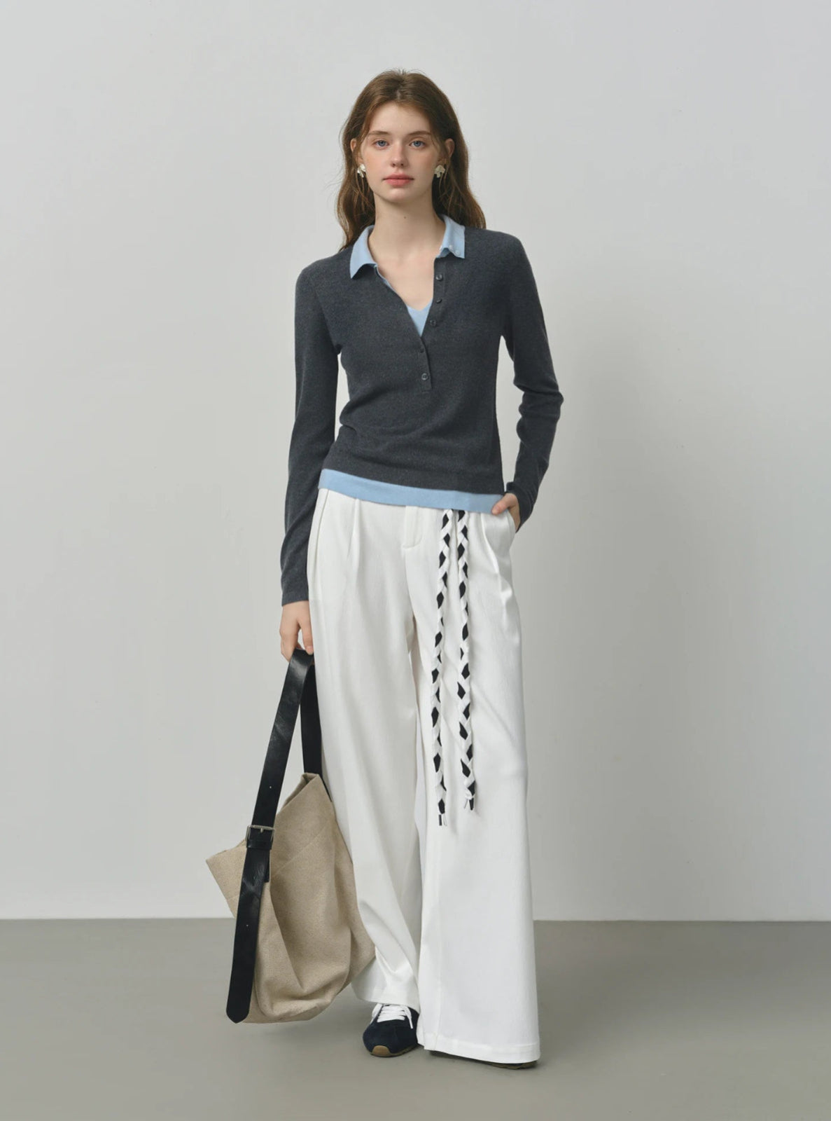 Woman wearing a dark long-sleeve top and white pants with lace details, holding a beige bag.