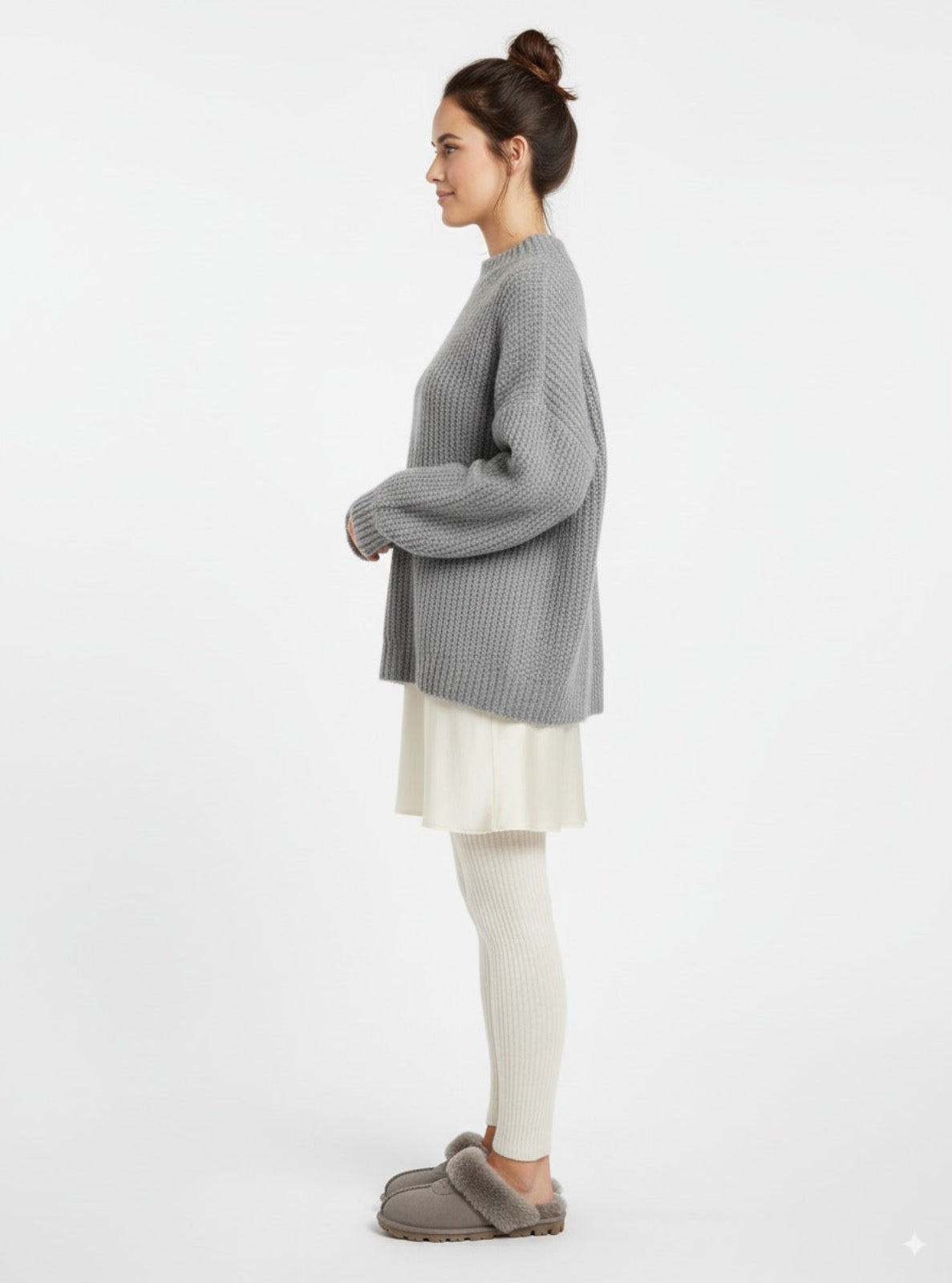 Woman wearing a gray sweater and white pants on a white background