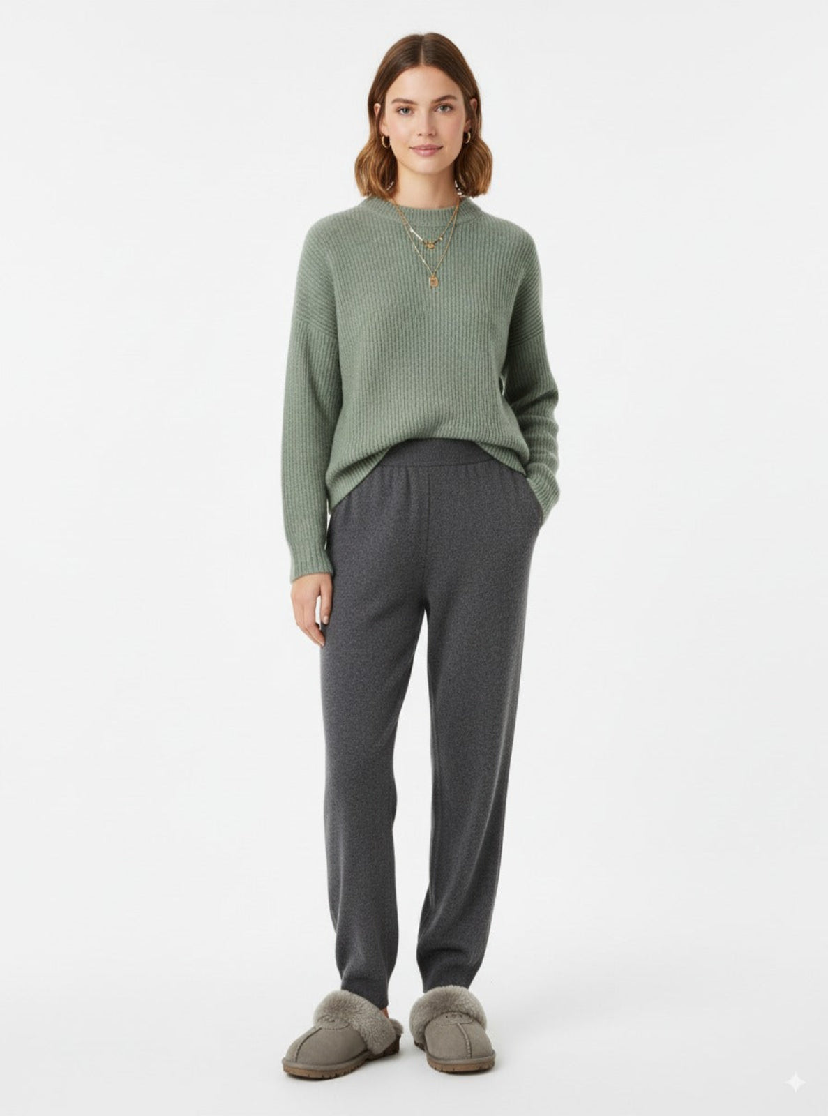 Woman wearing a green sweater and gray pants on a white background