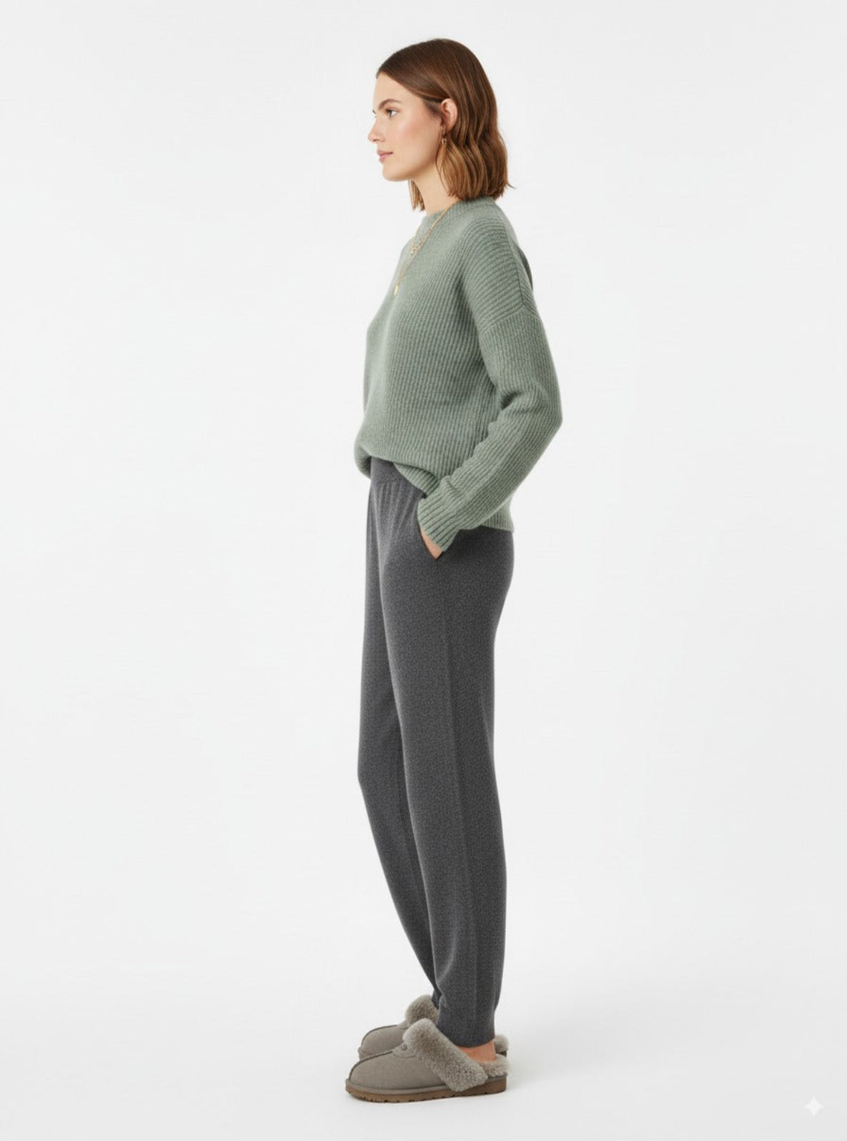 Woman wearing a green sweater and gray pants on a white background