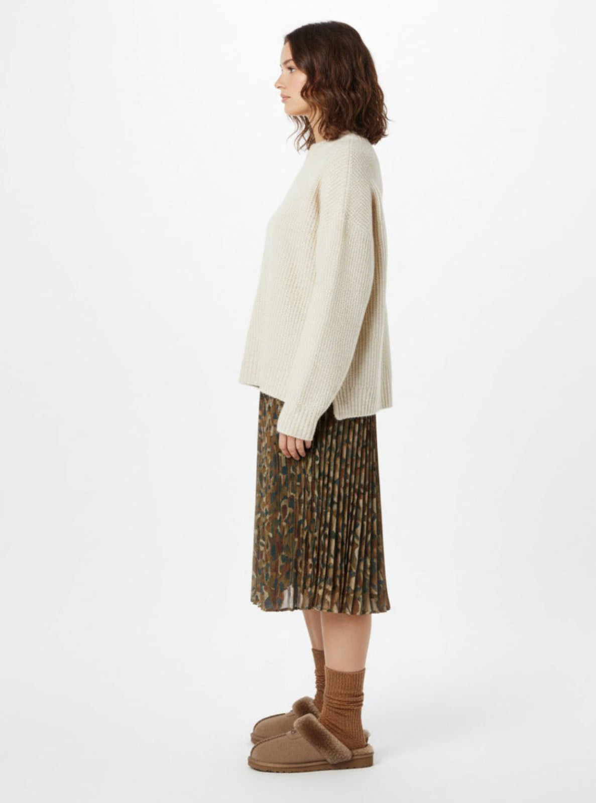 Woman wearing a cream sweater and patterned skirt with brown shoes on a white background