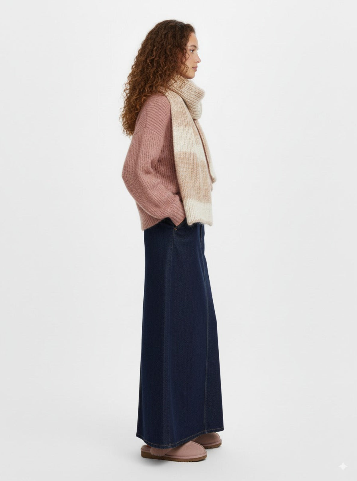 Woman wearing a pink sweater, beige scarf, and navy skirt on a white background