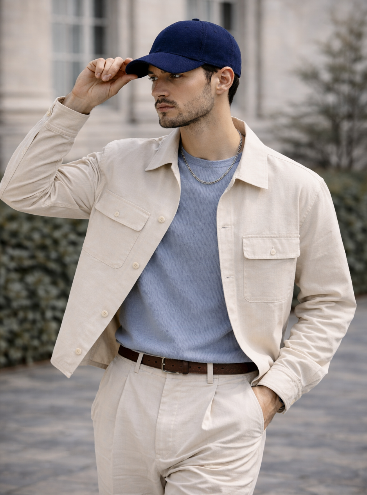 Man wearing a beige jacket, blue shirt, and cap outdoors.