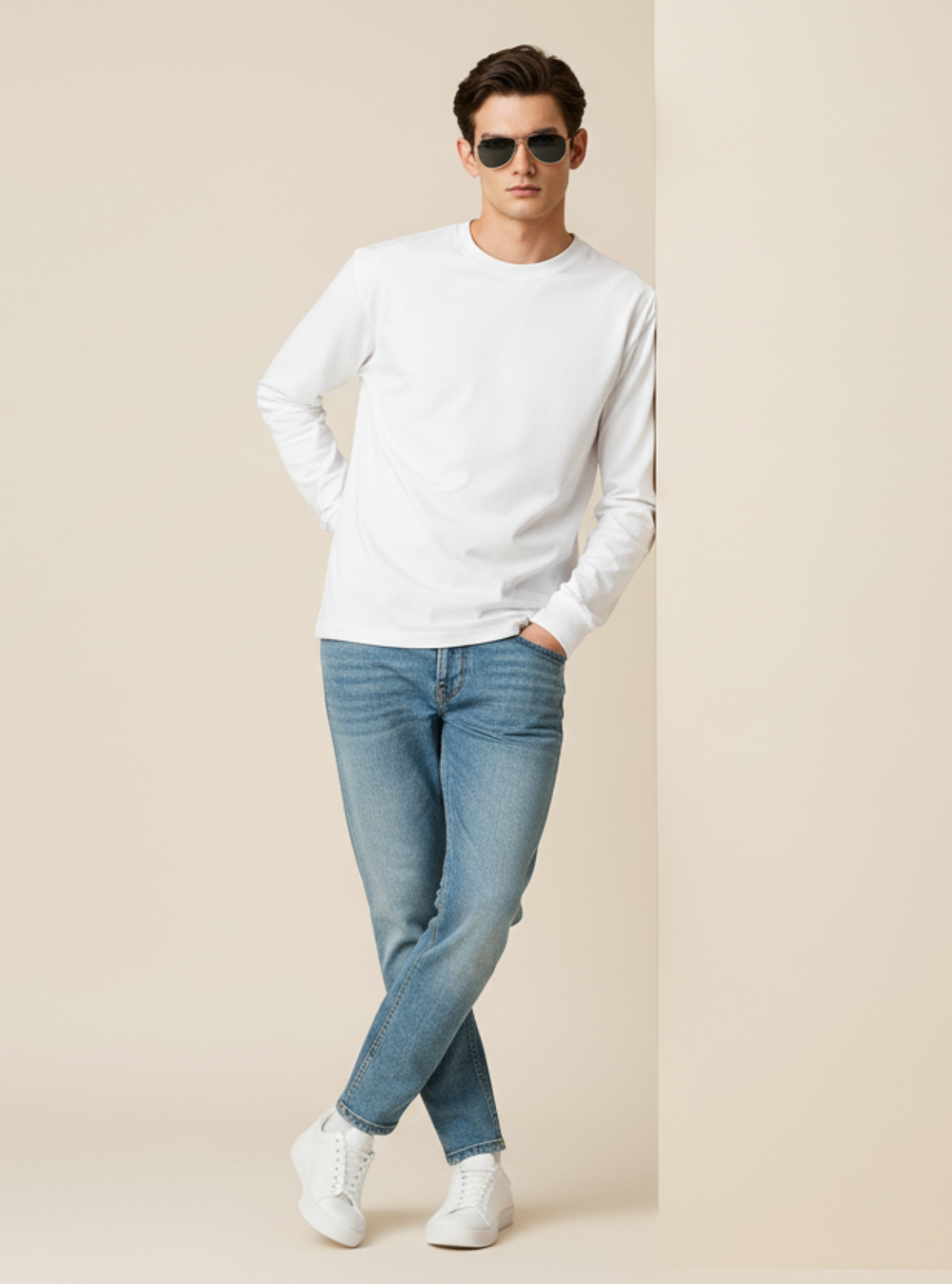 Man wearing a white sweater, light blue jeans, and white sneakers against a beige background