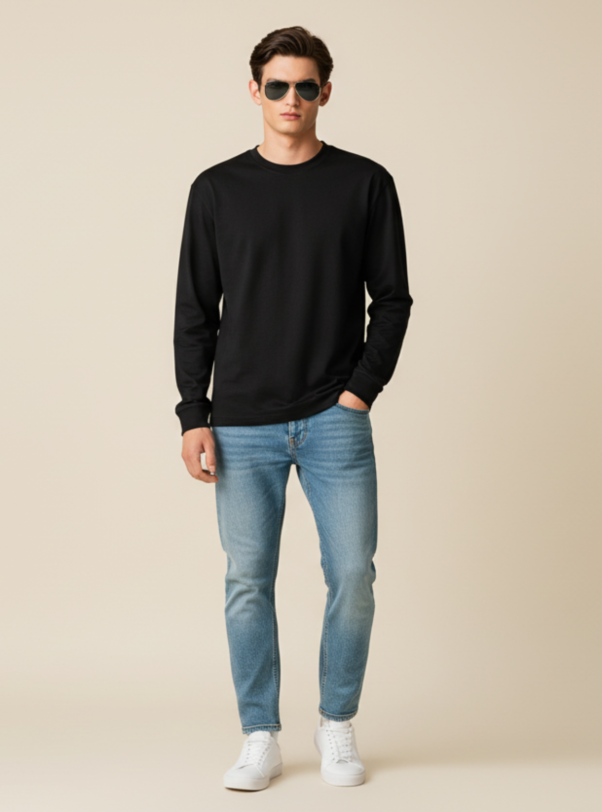 Man wearing a black sweater, light blue jeans, and white sneakers on a beige background