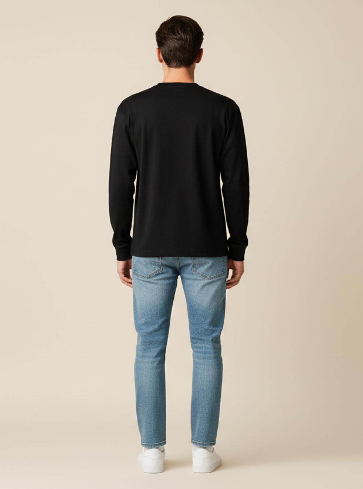 Man wearing a black long-sleeve shirt and light blue jeans on a beige background