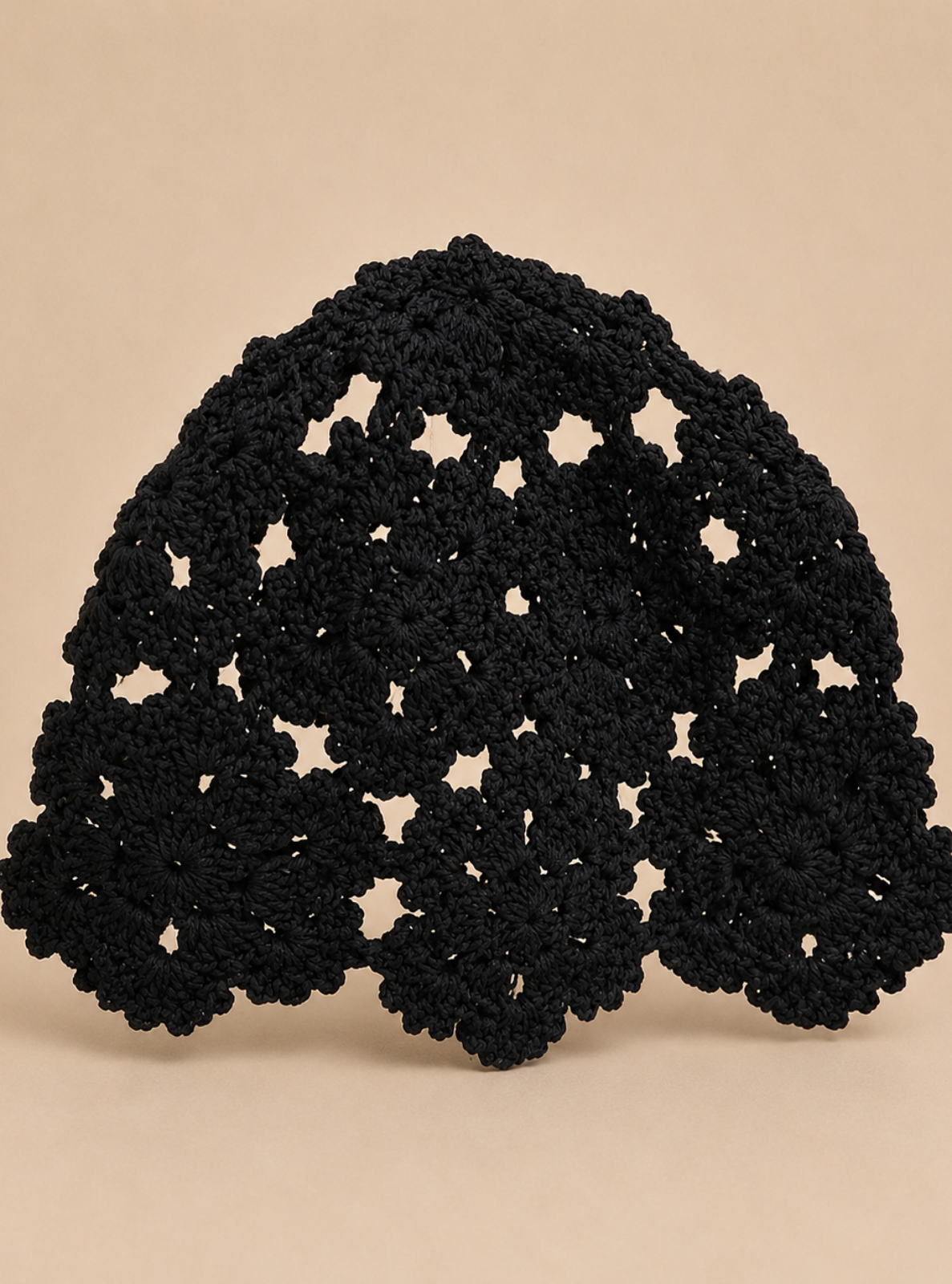 A black crocheted lace headband with a scalloped, floral pattern, displayed against a solid beige background.