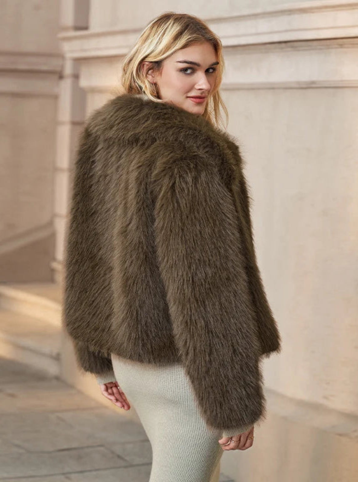Woman wearing a brown fur coat standing in front of a classical building.